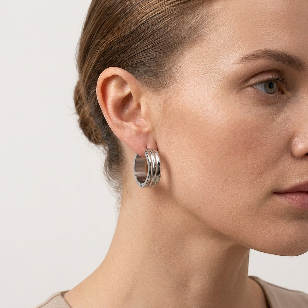 Aramat Jewels wide silver-tone stainless steel hoop earrings with triple stripe detail, worn by a woman.