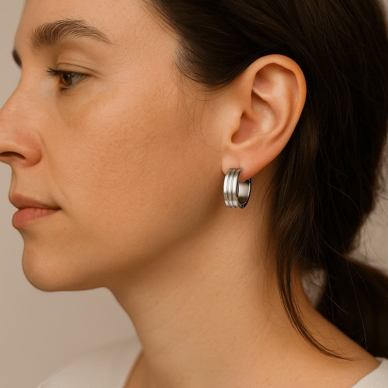 Aramat Jewels silver-tone stainless steel hoop earrings with three raised horizontal stripes, worn by a woman.