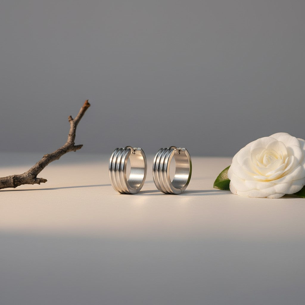 Aramat Jewels silver-tone stainless steel hoop earrings with three subtle vertical stripes, available in 13mm and 20mm diameters.