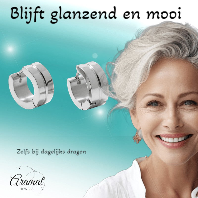 Aramat Jewels silver-tone stainless steel huggie hoop earrings with a subtle accent detail. Model wears them with a white top.