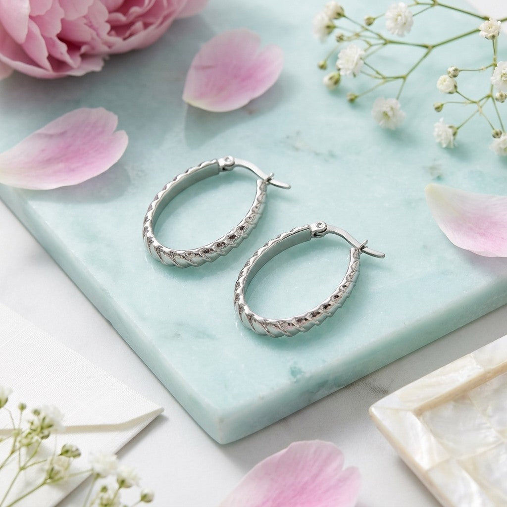 Aramat Jewels silver oval hoop earrings with diagonal stripe texture, 28mm diameter, made of stainless steel.