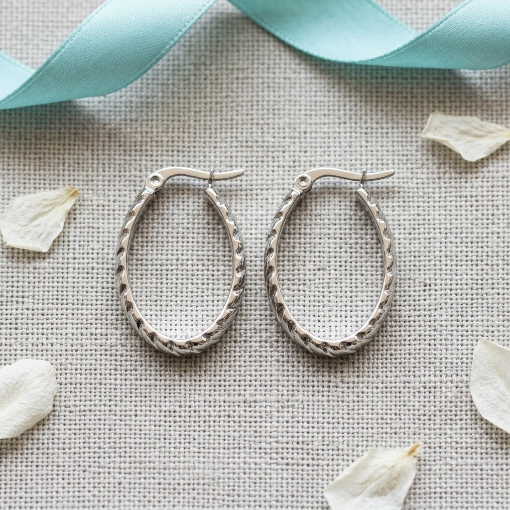 Aramat Jewels silver oval hoop earrings with diagonal stripe texture, 28mm diameter, made of stainless steel.