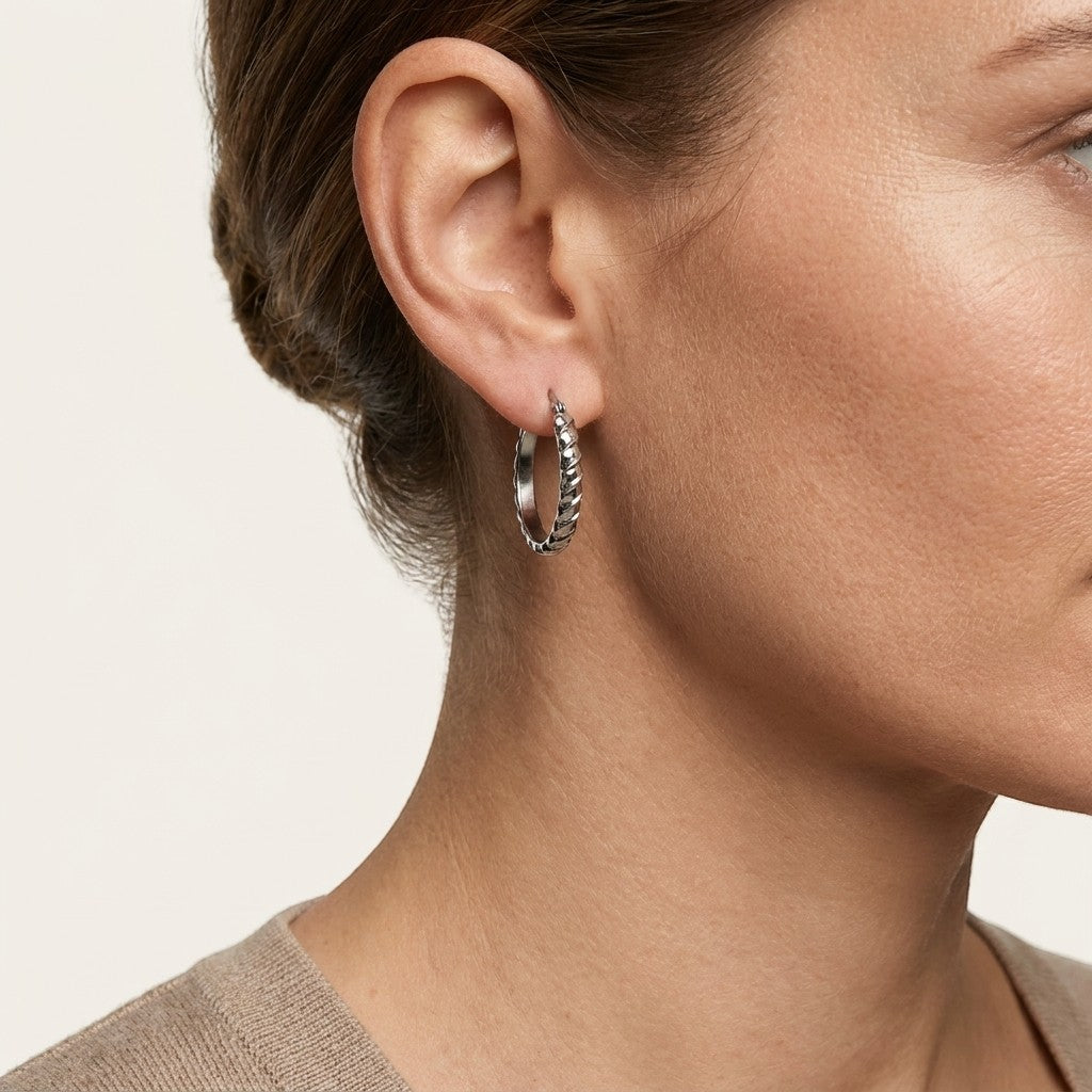 Aramat Jewels silver oval hoop earrings with diagonal stripe texture, 28mm diameter, worn by a model.