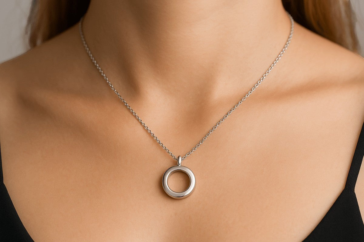 Aramat Jewels silver-colored 15mm round stainless steel cremation pendant on a delicate chain worn by a woman.
