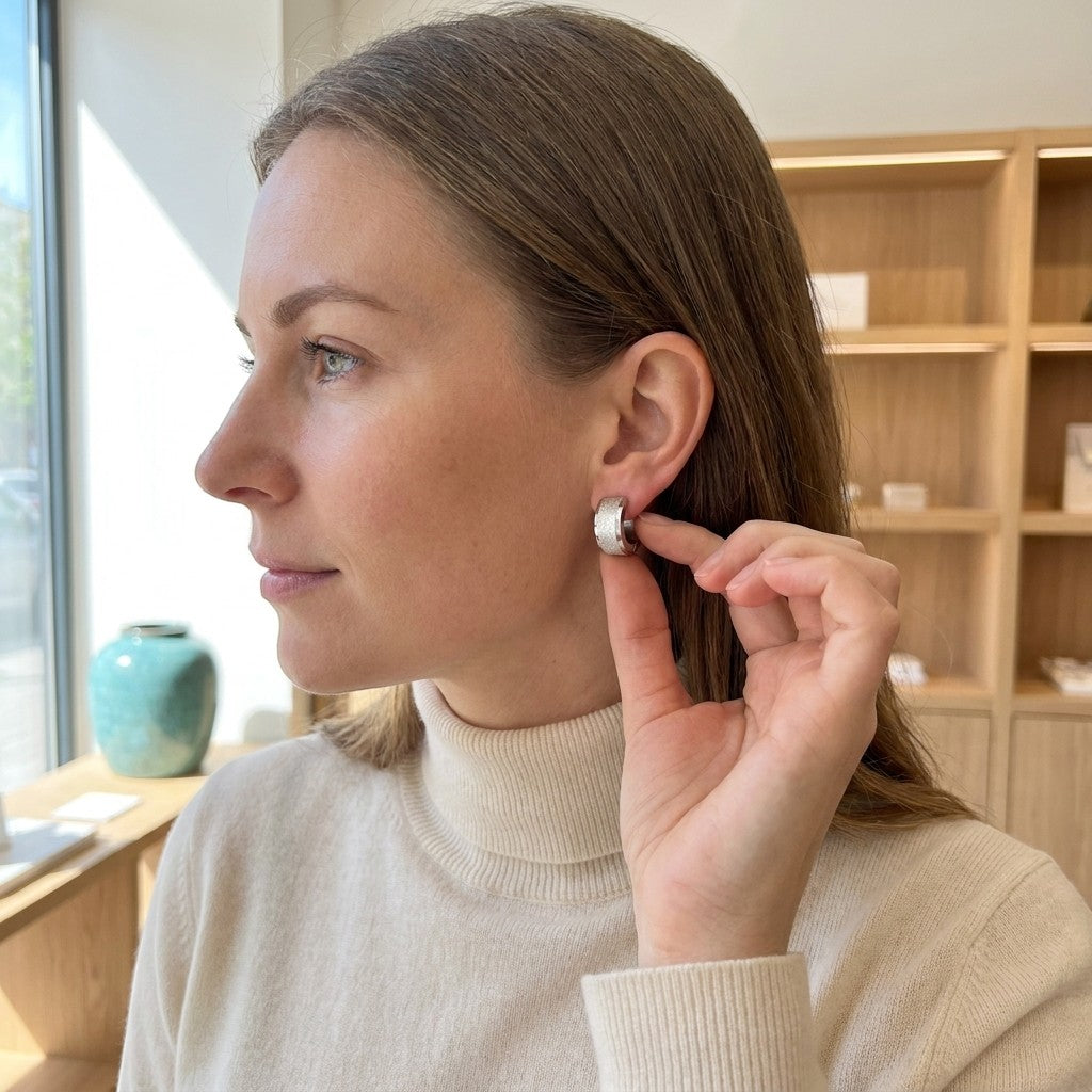 Aramat Jewels matte silver-colored RVS hoop earrings with sandblasted stripe detail, worn by a woman.