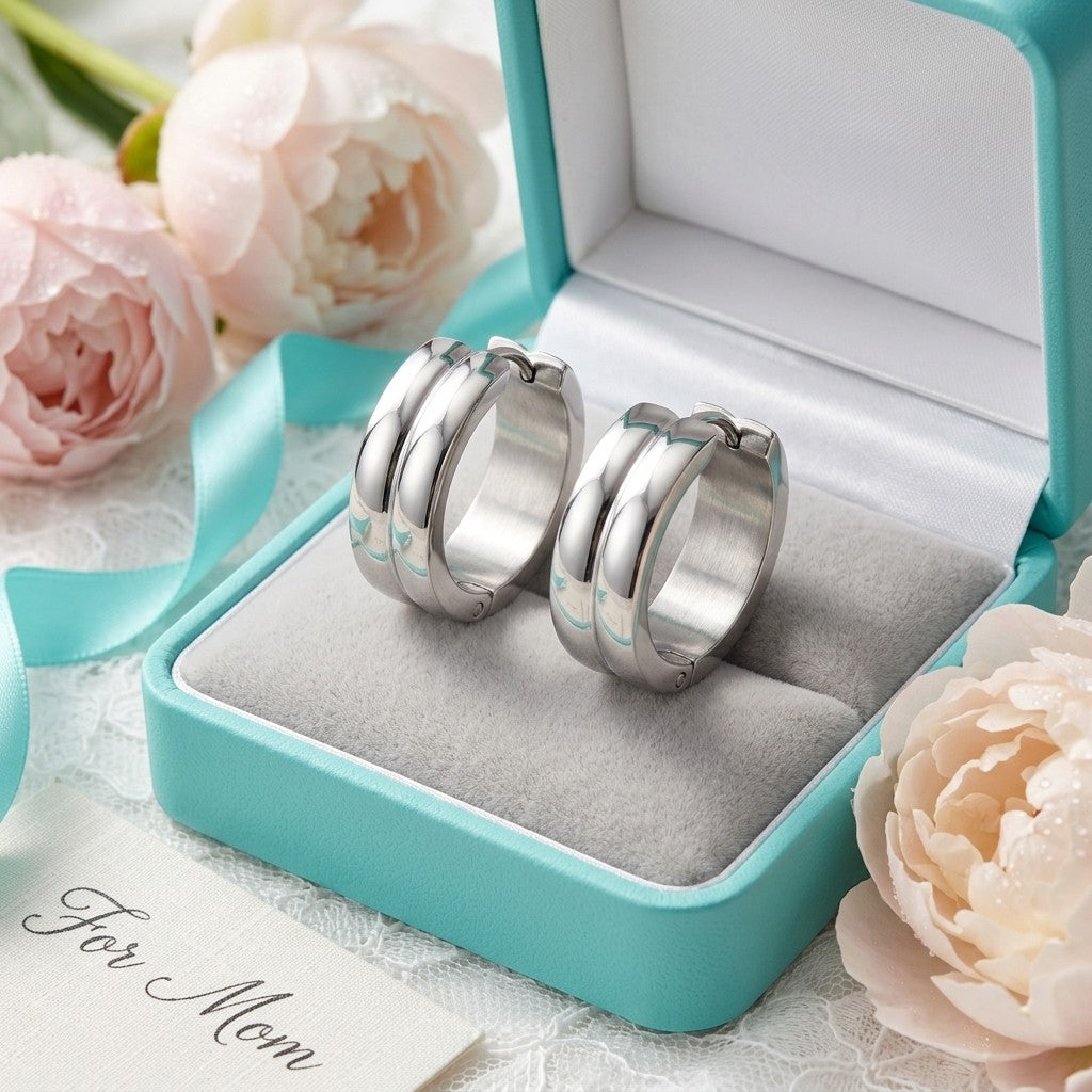 Aramat Jewels silver-tone stainless steel huggie hoop earrings with double stripe detail, presented in a teal jewelry box with soft pink roses.