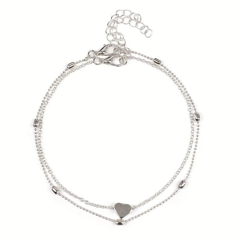 Aramat Jewels silver-colored steel anklet set featuring a delicate heart charm and small decorative beads.