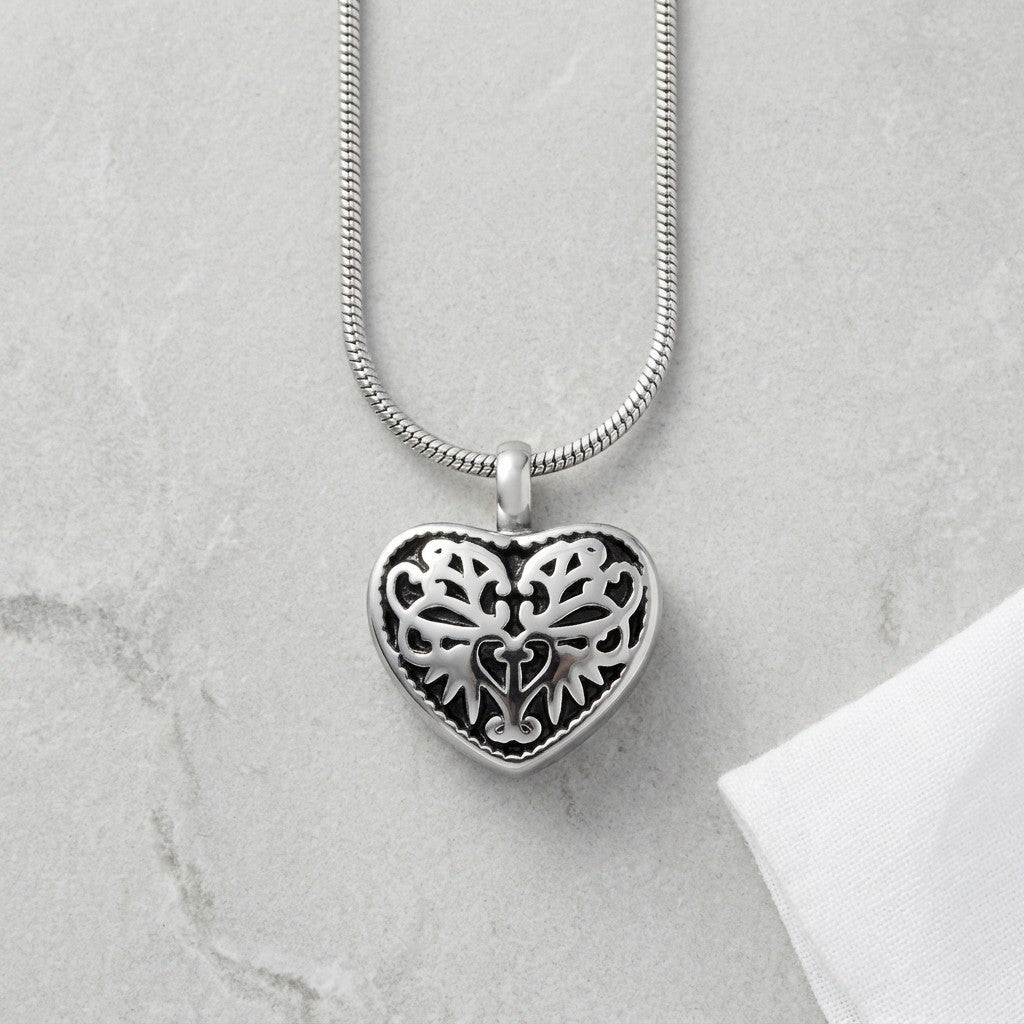 Aramat Jewels silver-tone steel heart-shaped cremation pendant with black enamel inlay and ornate filigree design.