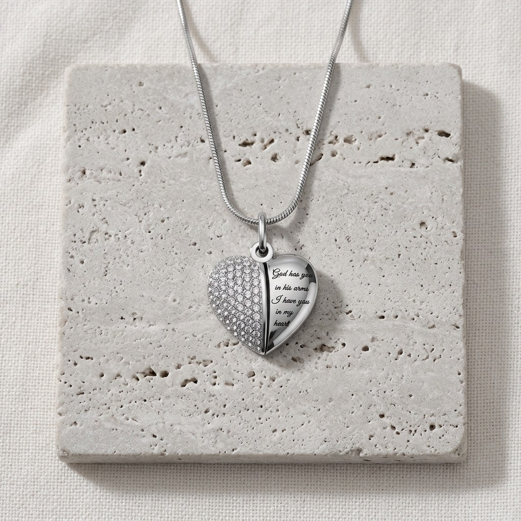 Aramat Jewels zilverkleurige stalen hartvormige ashanger met lila kristallen en gravure 'God has you in his arms, I have you in my heart'.