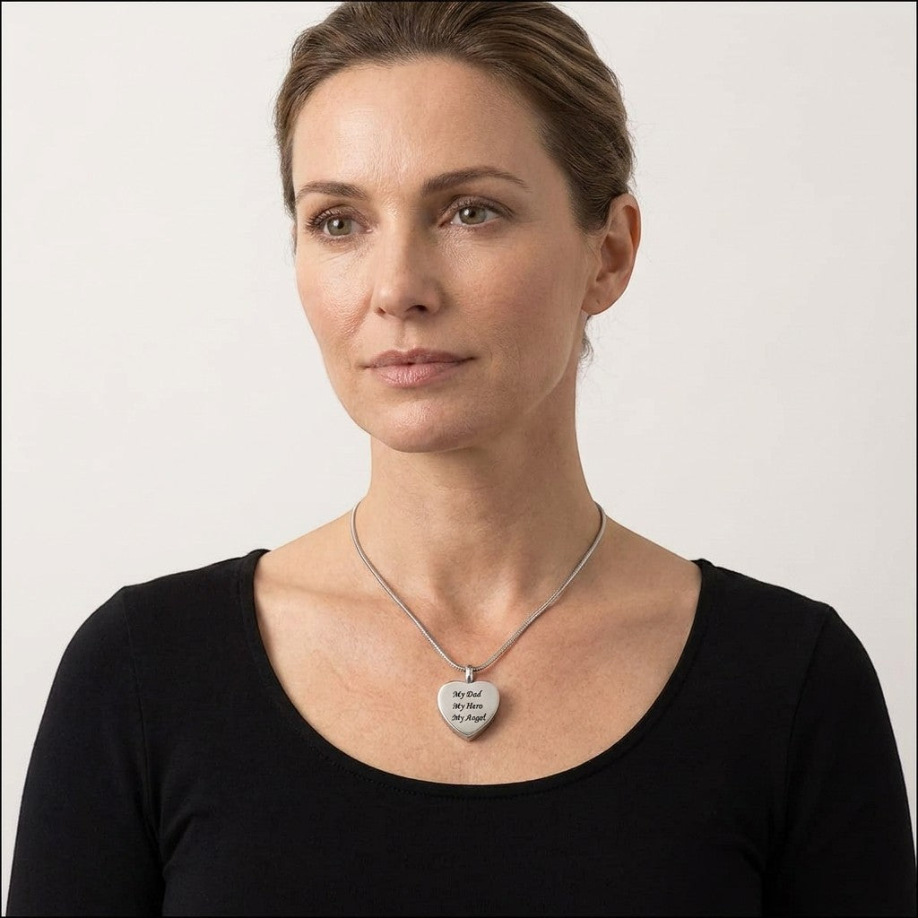Aramat Jewels stalen hartvormige crematiehanger met gravure 'My Dad My Hero My Angel'. Gedragen door een vrouw met zwarte top.