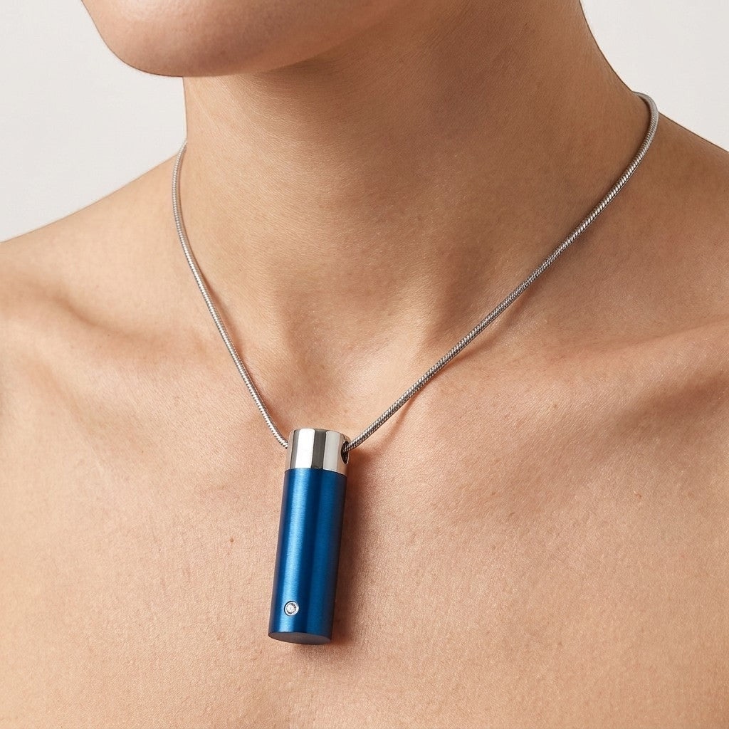 Aramat Jewels stalen blauwe cilinder ashanger met een klein diamantje, gedragen aan een zilverkleurige slangenhalsketting.