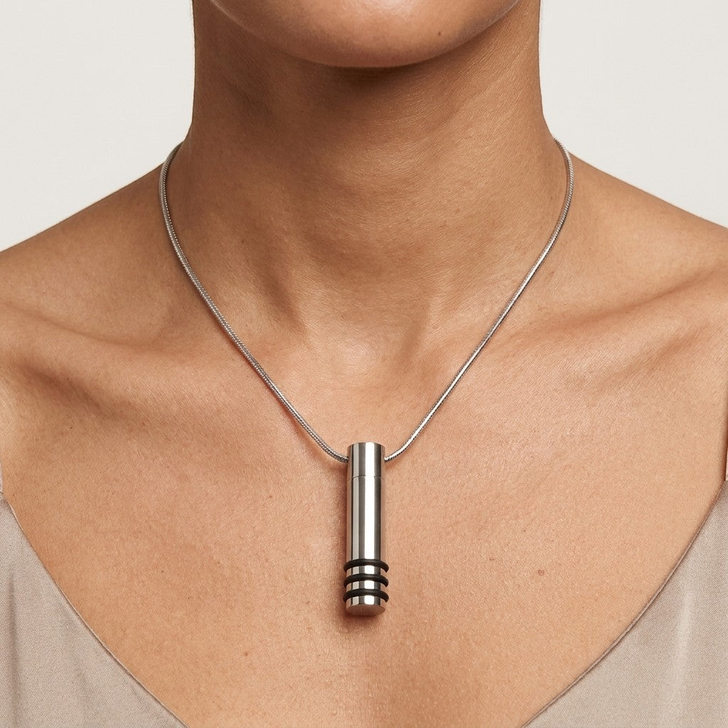 Aramat Jewels® zilverkleurige stalen cilinder ashanger met zwarte strepen, 38x10mm, gedragen aan een slangenketting.