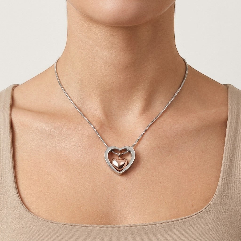 Aramat Jewels stalen hart crematiehanger in zilverkleurig en rosékleurig, gedragen door een model.