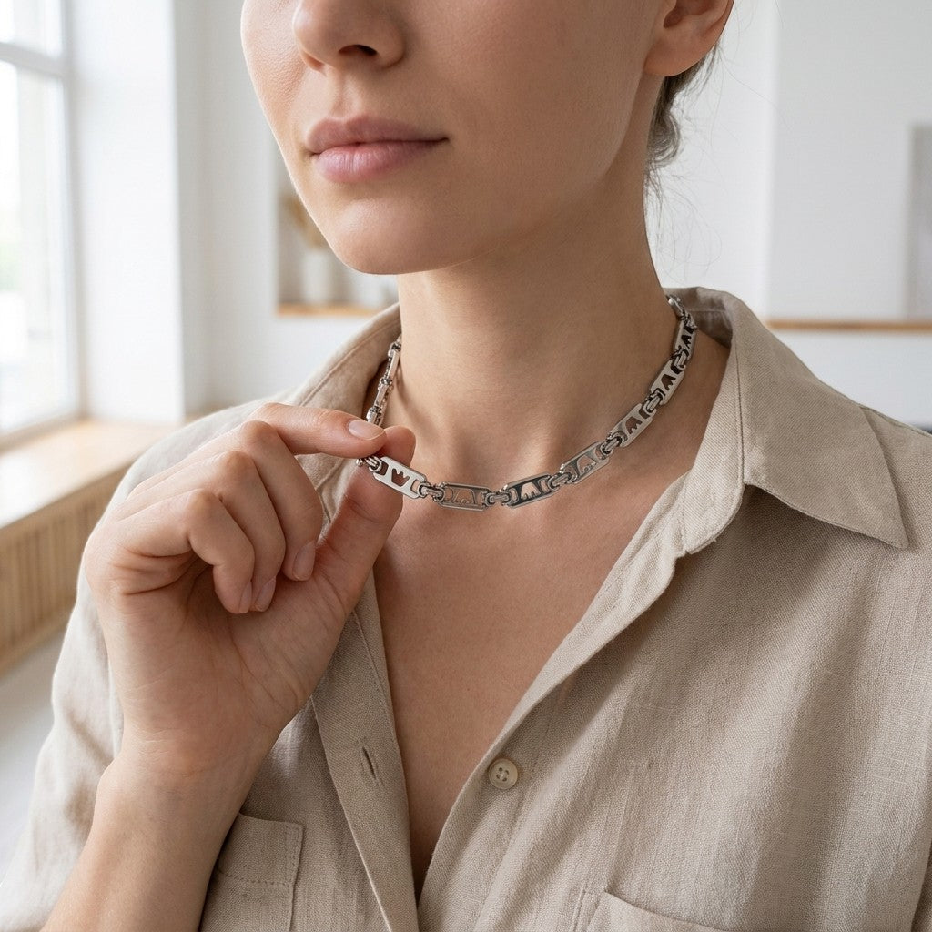 Aramat Jewels brede zilverkleurige stalen koningsketting met kroonmotief gedragen door een model in een beige overhemd.