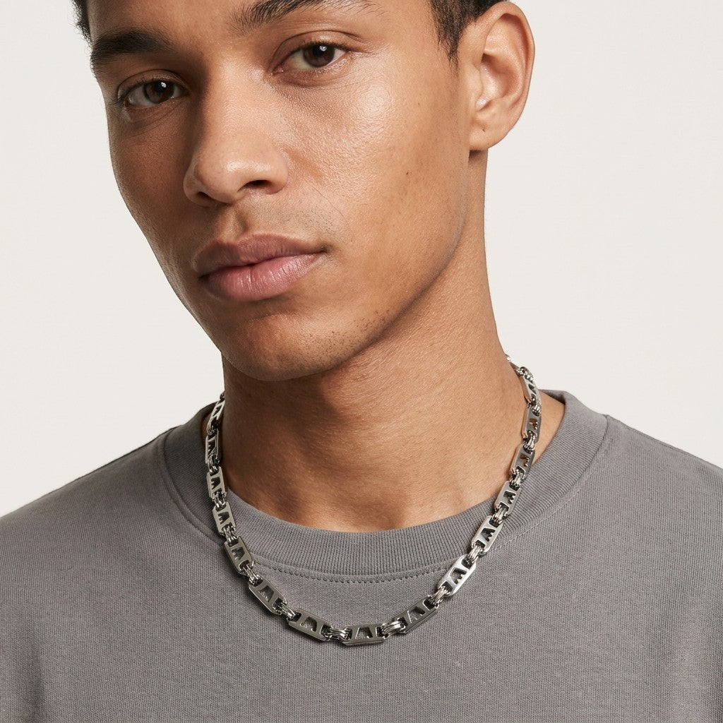Aramat Jewels brede zilverkleurige stalen koningsketting met kroonmotief gedragen door een man in een grijs shirt.