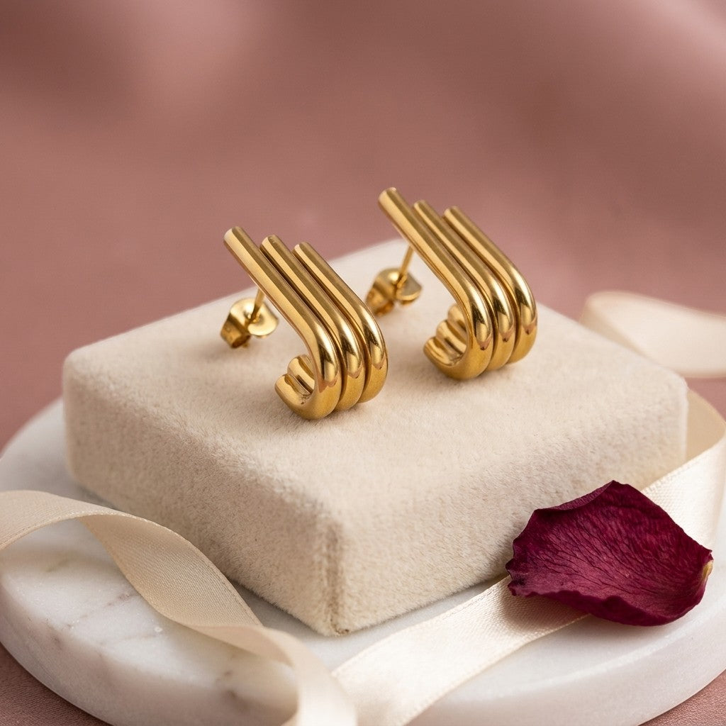 Aramat Jewels goudkleurige triple oorstekers met drie staafjes in een halve hoepel design op een marmeren ondergrond.