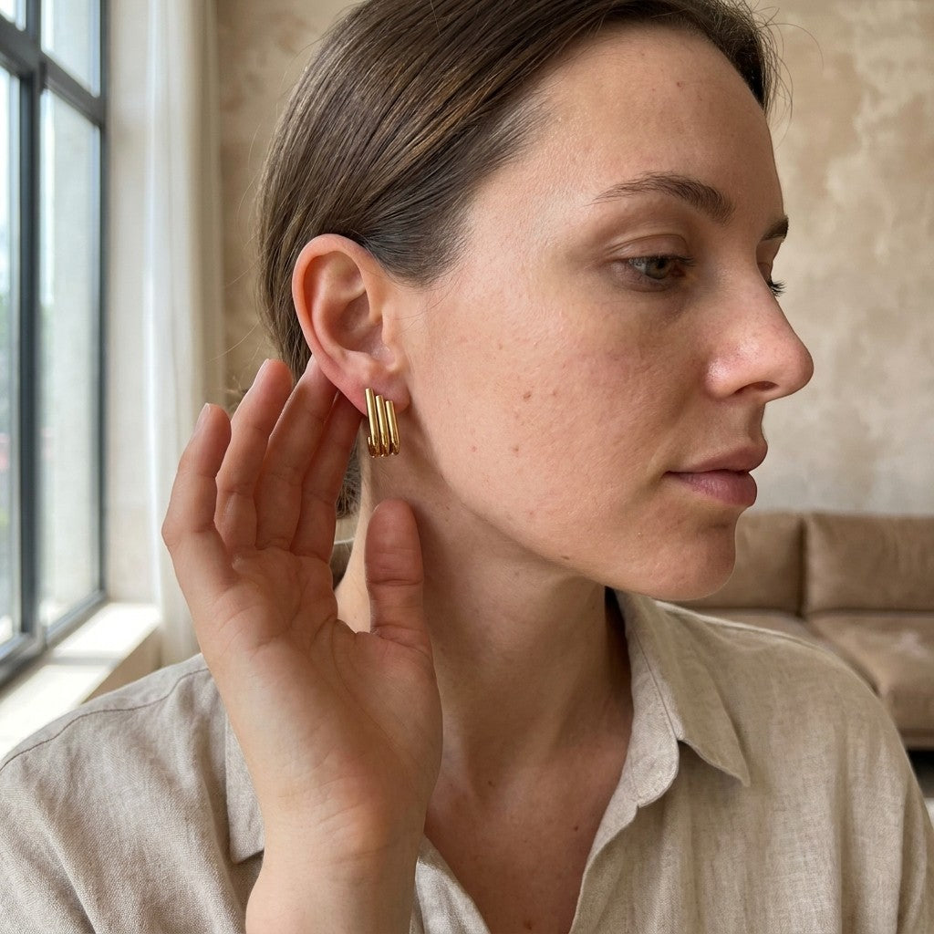 Aramat Jewels goudkleurige triple oorstekers met drie staafjes in een halve hoepel design gedragen door een vrouw.