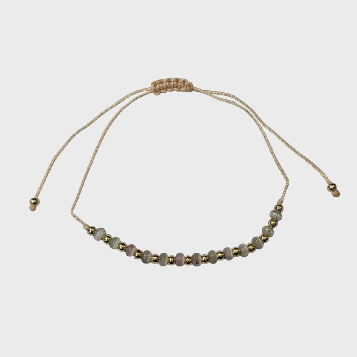 Aramat Jewels verstelbaar enkelbandje met glanzende cats eye kralen en goudkleurige accenten op beige touw.