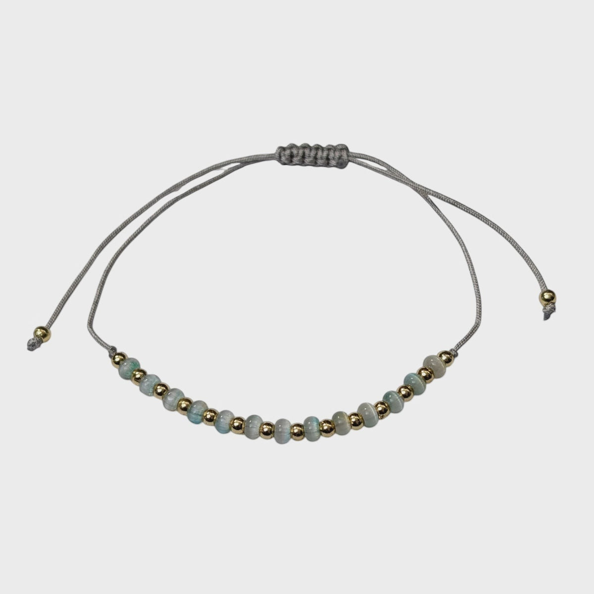 Aramat Jewels verstelbaar enkelbandje met grijze cats eye kralen en goudkleurige accenten op een grijs touwtje.