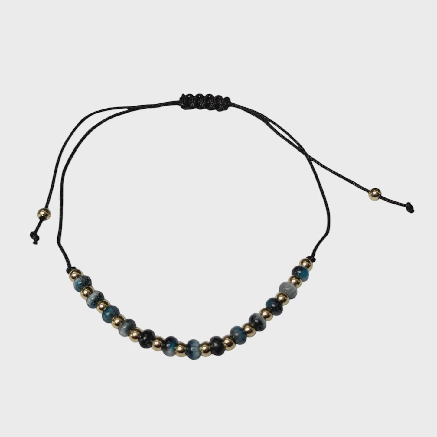 Aramat Jewels verstelbaar enkelbandje met blauwe cats eye kralen en gouden accenten op een zwart touwtje.