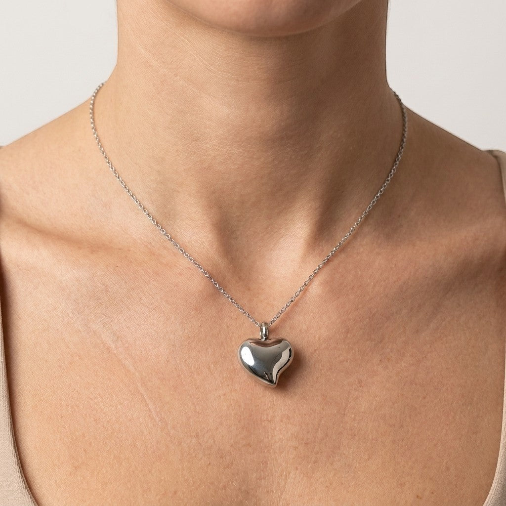 Aramat Jewels zilverkleurige hartvormige crematiehanger van roestvrij staal, gedragen aan een fijne ketting.