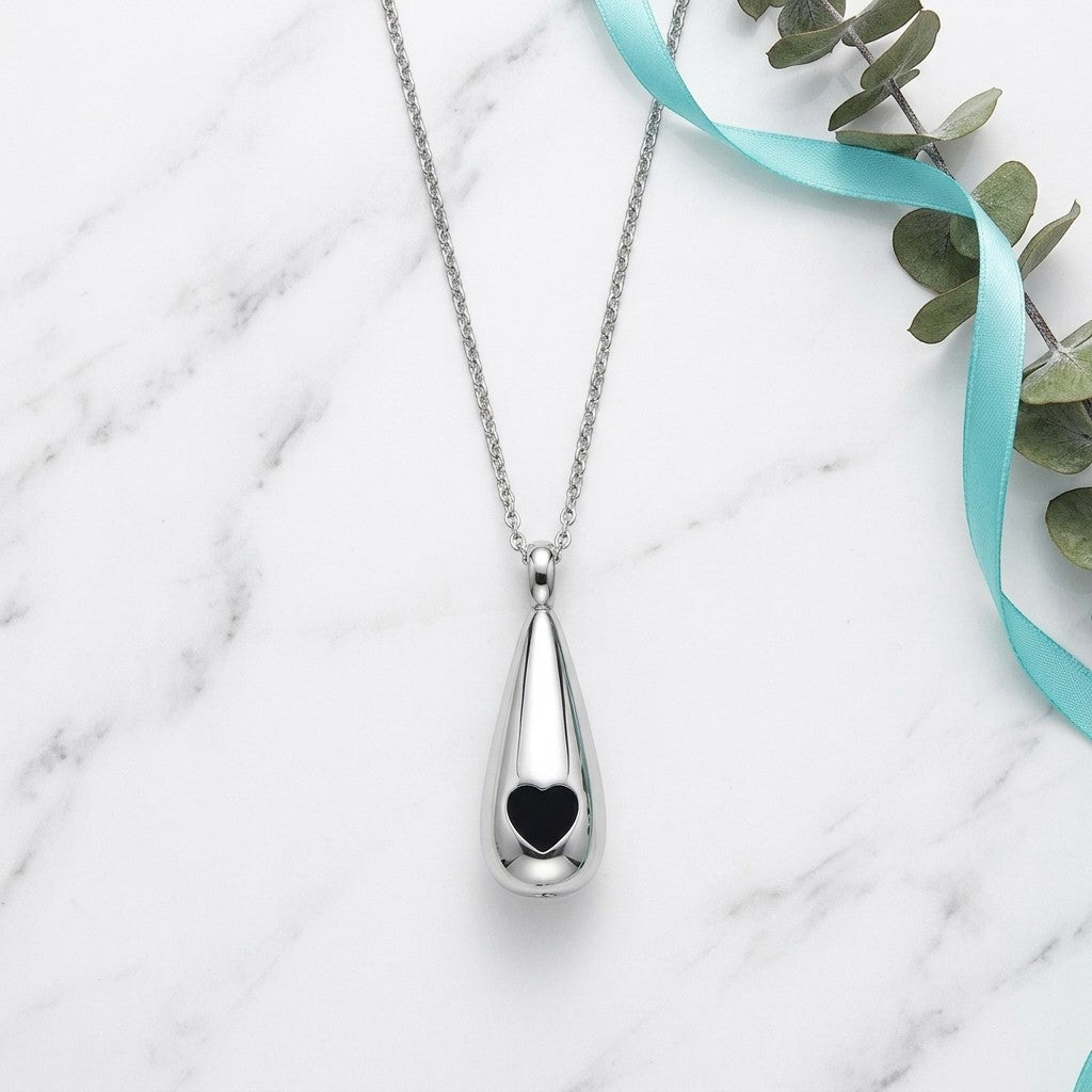Aramat Jewels zilverkleurige druppelvormige ashanger met zwart hart, gemaakt van roestvrij staal.