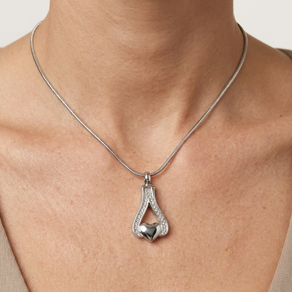 Aramat Jewels zilverkleurige stalen ashanger in hartvorm met kristallen, gedragen aan een slangenhalsketting.