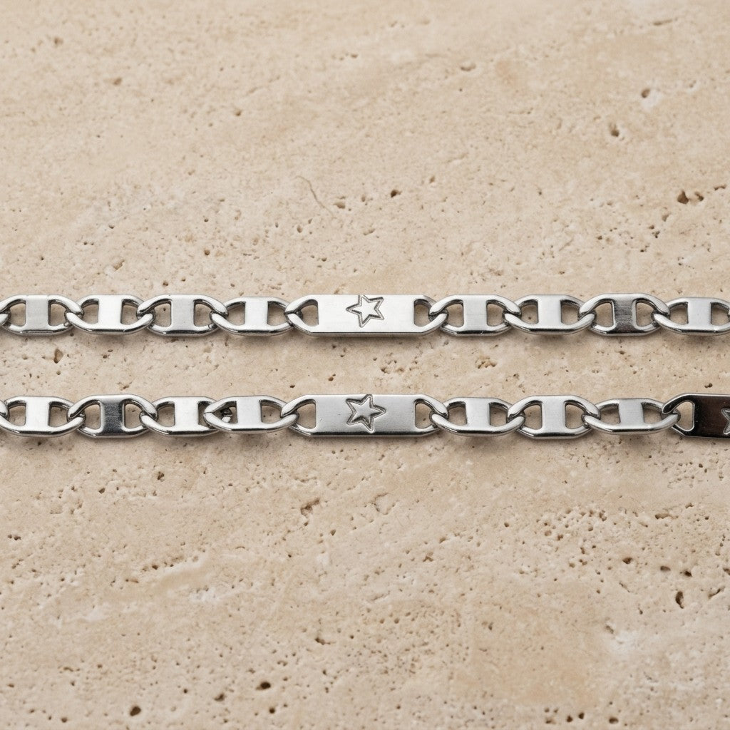 Aramat Jewels zilverkleurige stalen marine schakel ketting met sterretjes detail op een beige stenen ondergrond.