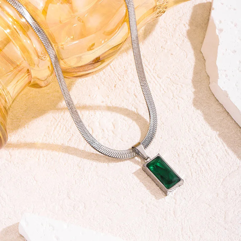 Aramat Jewels zilverkleurige platte slangenketting met een rechthoekige groene zirkonia hanger op een lichte ondergrond.
