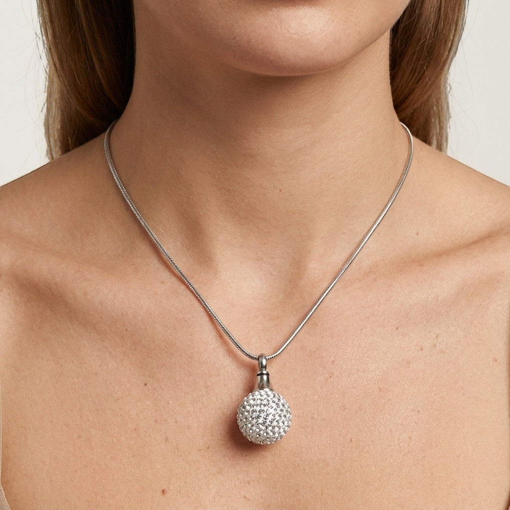 Aramat Jewels® zilverkleurige stalen ashanger in bolvorm, bezet met kristallen, gedragen aan een slangenketting.