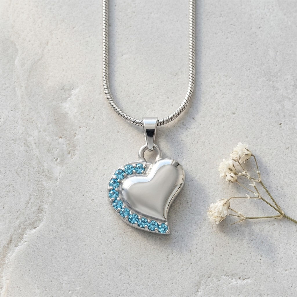 Aramat Jewels zilverkleurige stalen ashanger in hartvorm met blauwe zirkonia steentjes. Een elegant gedenksieraad.