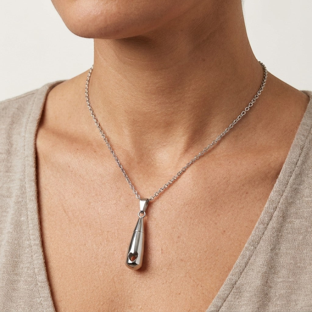 Aramat Jewels zilverkleurige stalen druppelvormige ashanger met opengewerkt hartje, gedragen door een model.