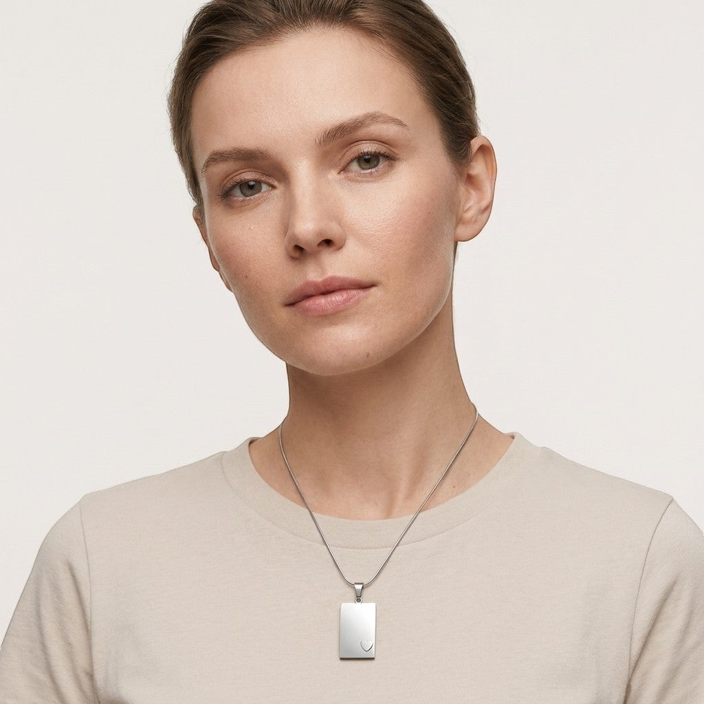 Aramat Jewels zilverkleurige stalen rechthoekige ashanger met klein hartje, gedragen door een vrouw.