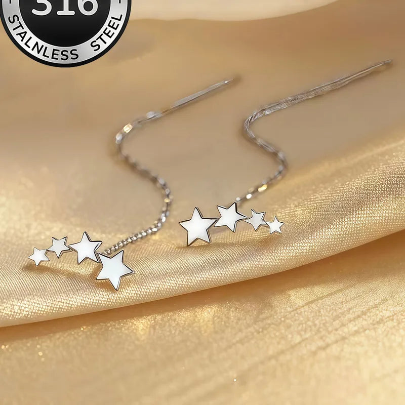 Aramat Jewels zilverkleurige doortrek oorbellen van RVS met drie sterretjes aan een fijne ketting op een satijnen stof.