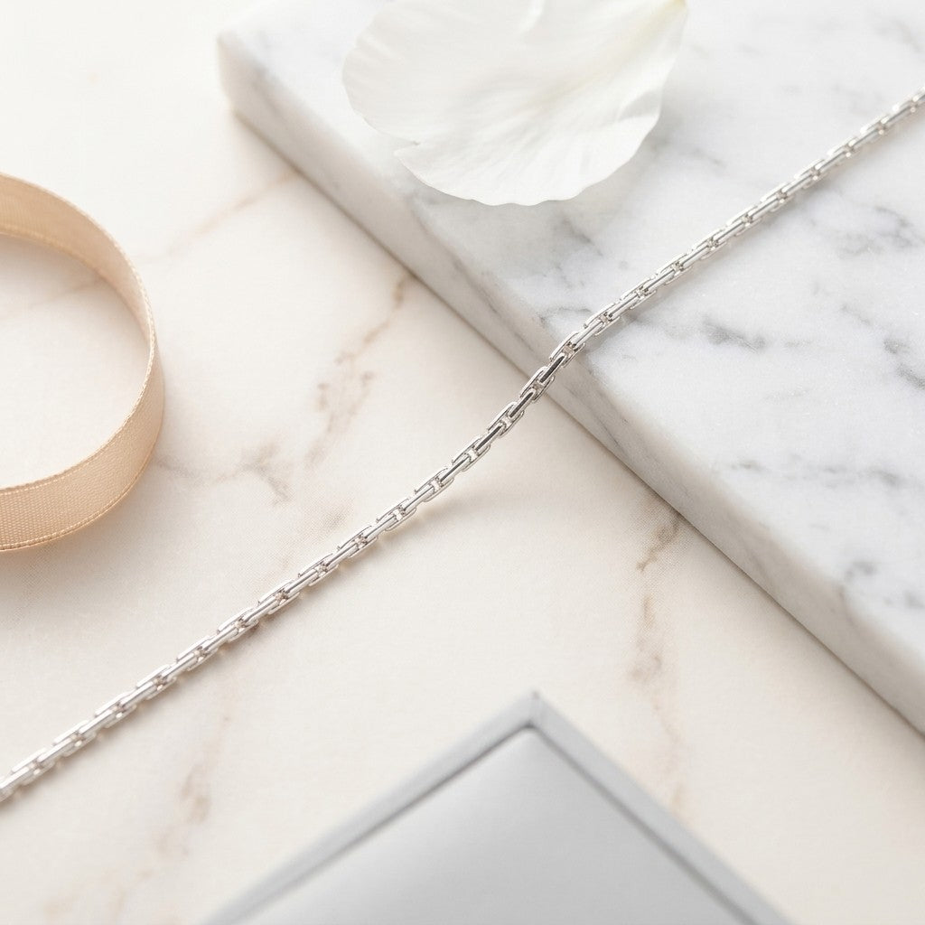 Aramat Jewels zilverkleurige slangenketting van roestvrij staal op een marmeren ondergrond met een bloemblad.