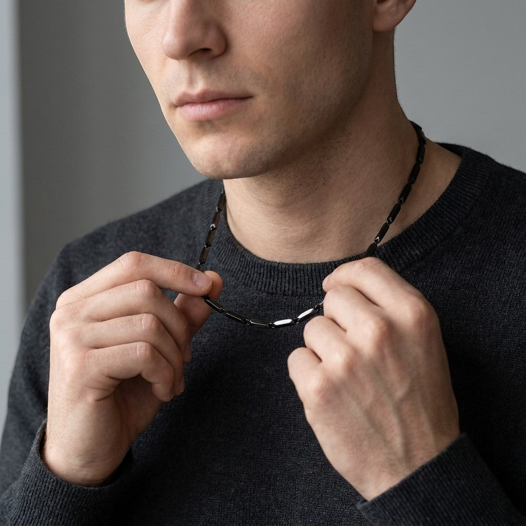 Aramat Jewels zwarte bamboo schakelketting van roestvrij staal gedragen door een man in een grijze trui.