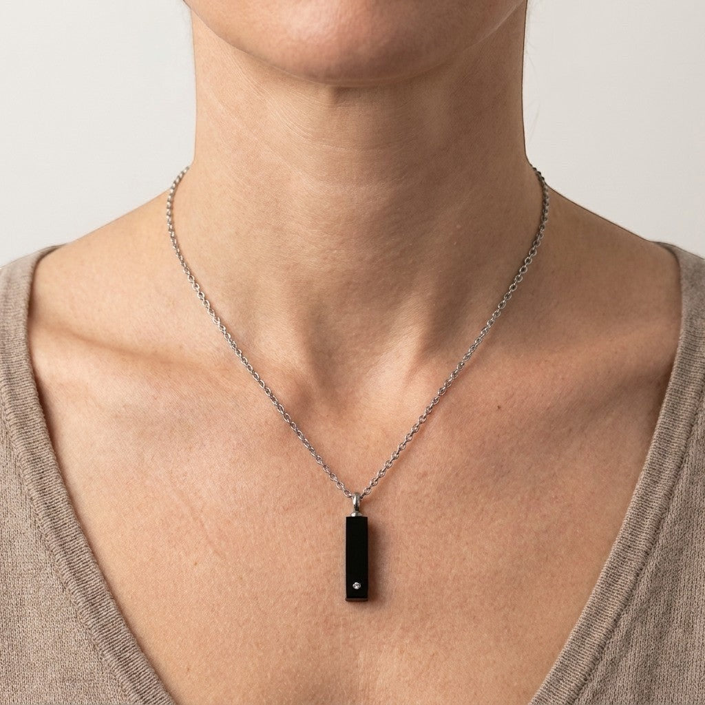 Aramat Jewels zwarte buis ashanger van 316L staal met een kristal, gedragen aan een zilverkleurige ketting.