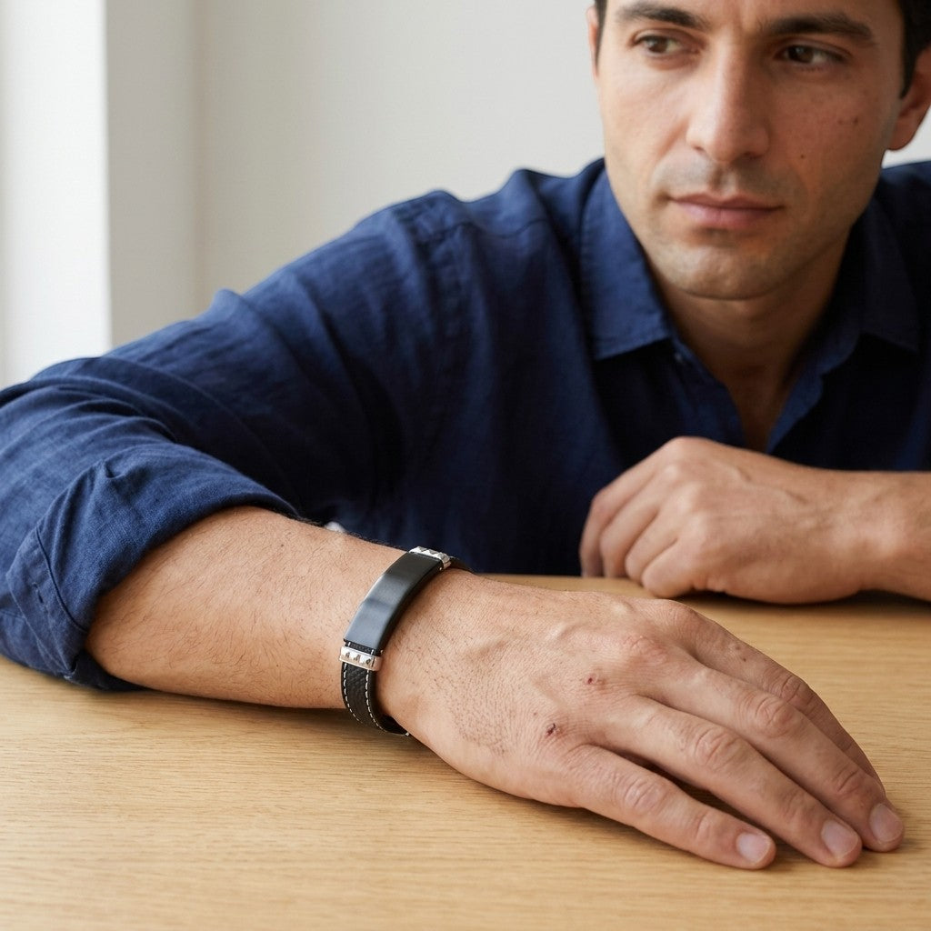 Aramat Jewels zwarte leren herenarmband met graveerbare stalen plaat en wit stiksel gedragen door een man.