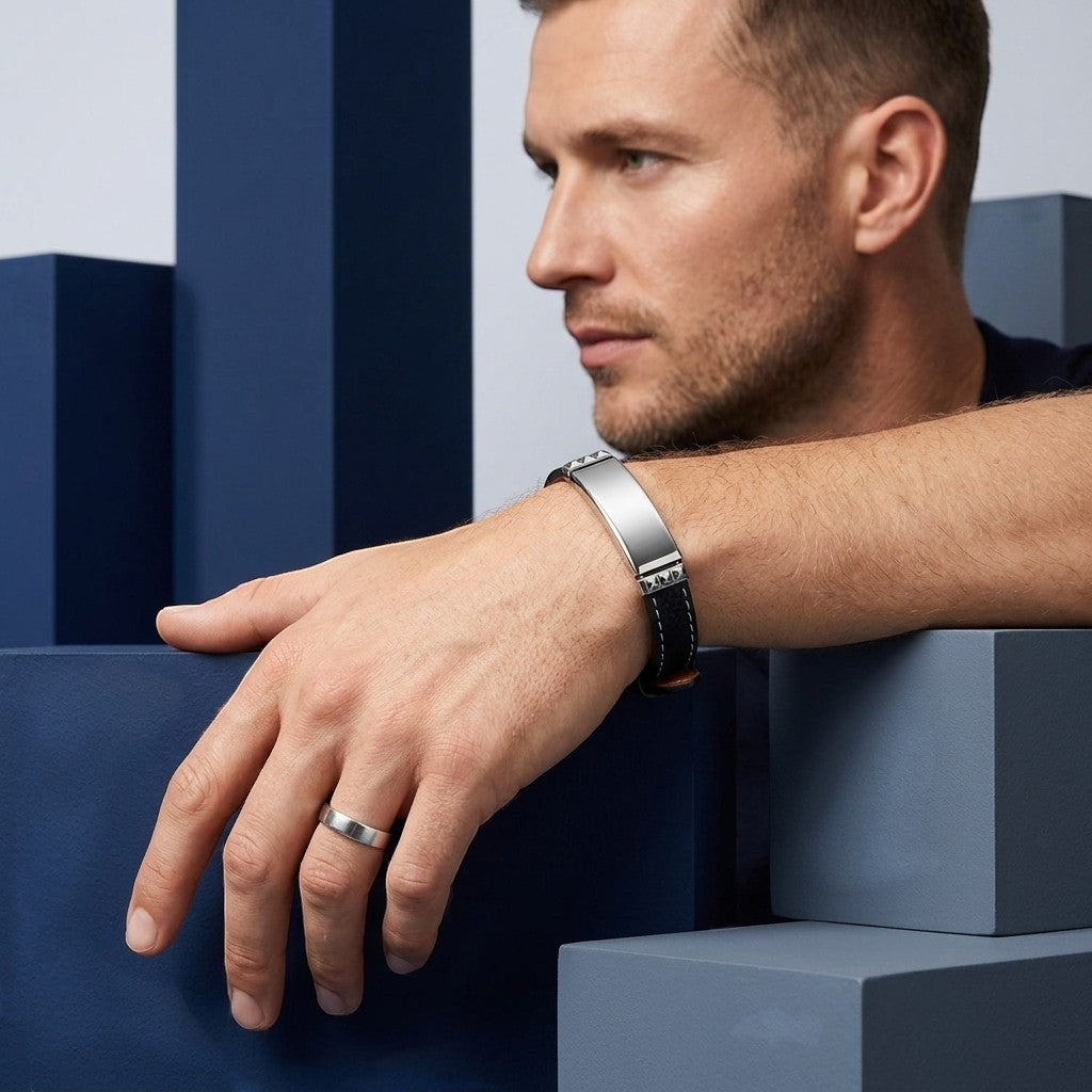 Aramat Jewels zwarte leren herenarmband met graveerbare zilverkleurige stalen plaat en wit stiksel om een pols.