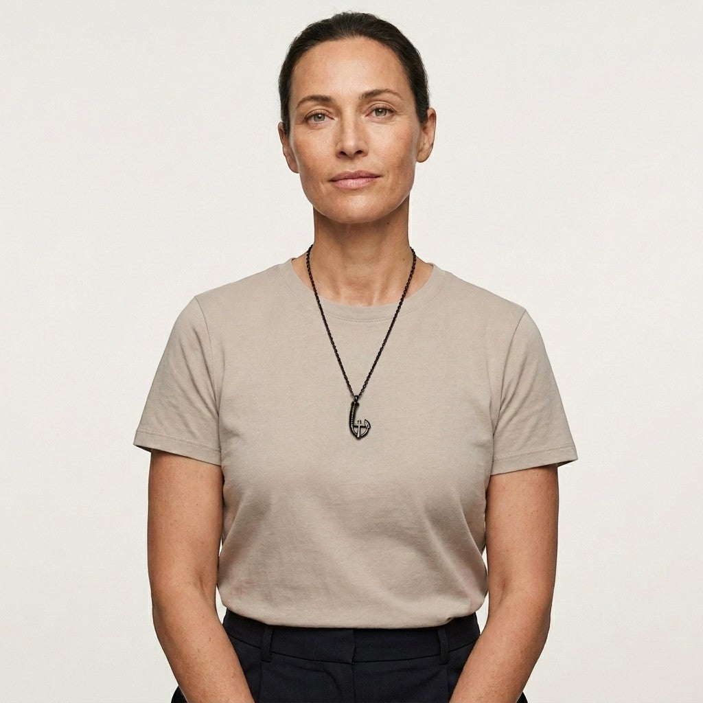 Aramat Jewels zwarte stalen ashanger in vishaakvorm met kruisje, gedragen door een vrouw met een beige T-shirt.