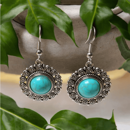 Paar sierlijke zilveren oorbellen met turquoise edelstenen in een cirkelvormig ontwerp.