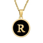 Gouden hangerketting met de letter ’R’ op een zwarte ronde achtergrond.