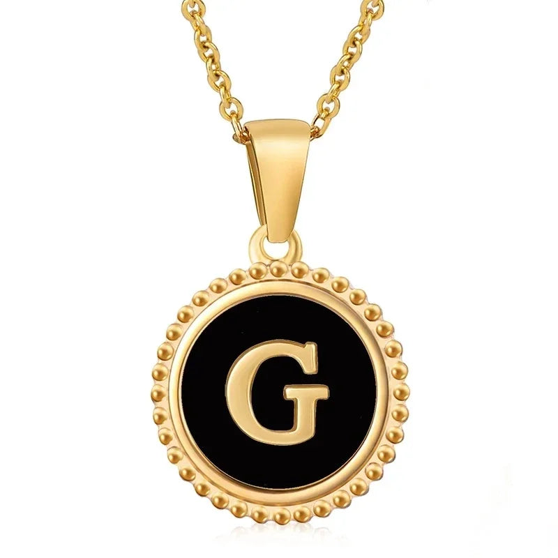 Hanger met vergulde ketting met de letter ’G’ op een zwarte ronde achtergrond met kralenrand.