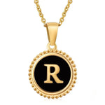 Hanger met vergulde ketting met de letter ’R’ op een zwarte ronde achtergrond met kralenrand.