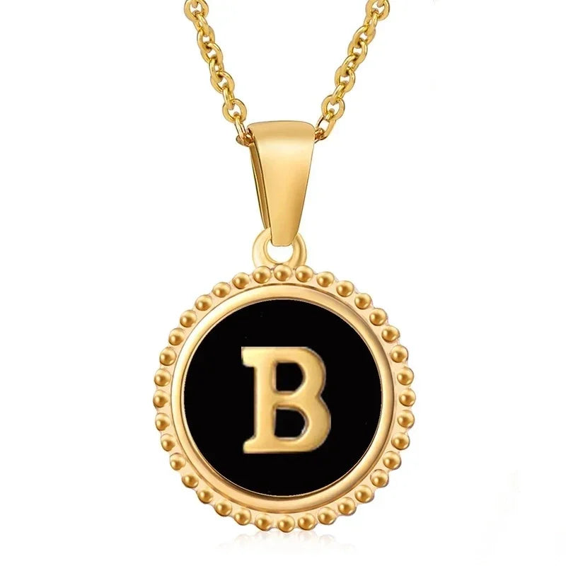 Hanger met vergulde ketting met de letter ’B’ op een zwarte ronde achtergrond met kralenrand.