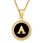 Hanger met vergulde ketting met de letter ’A’ op een zwarte ronde achtergrond met kralenrand.