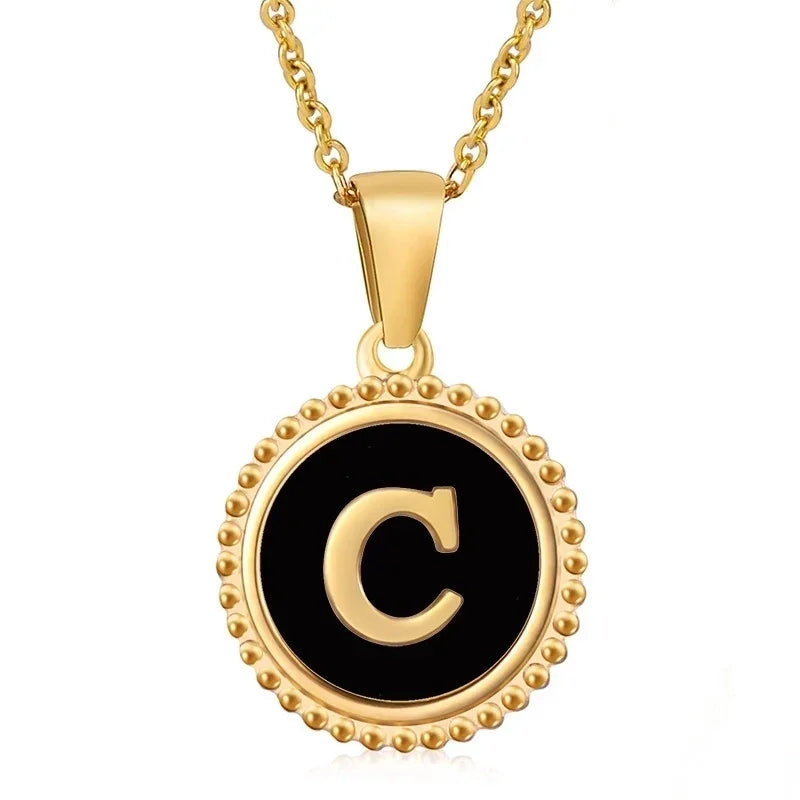 Hanger met vergulde ketting met de letter ’C’ op een zwarte ronde achtergrond met kralenrand.