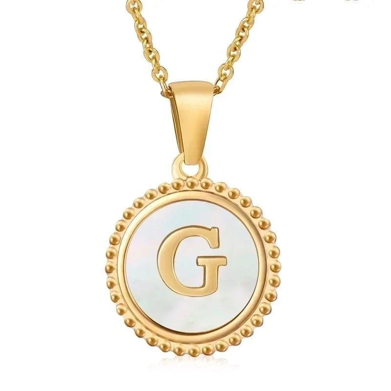 Hanger met vergulde ketting met de letter ’G’ op een witte ronde achtergrond met kralenrand.