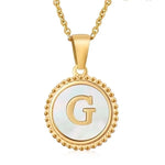 Hanger met vergulde ketting met de letter ’G’ op een witte ronde achtergrond met kralenrand.