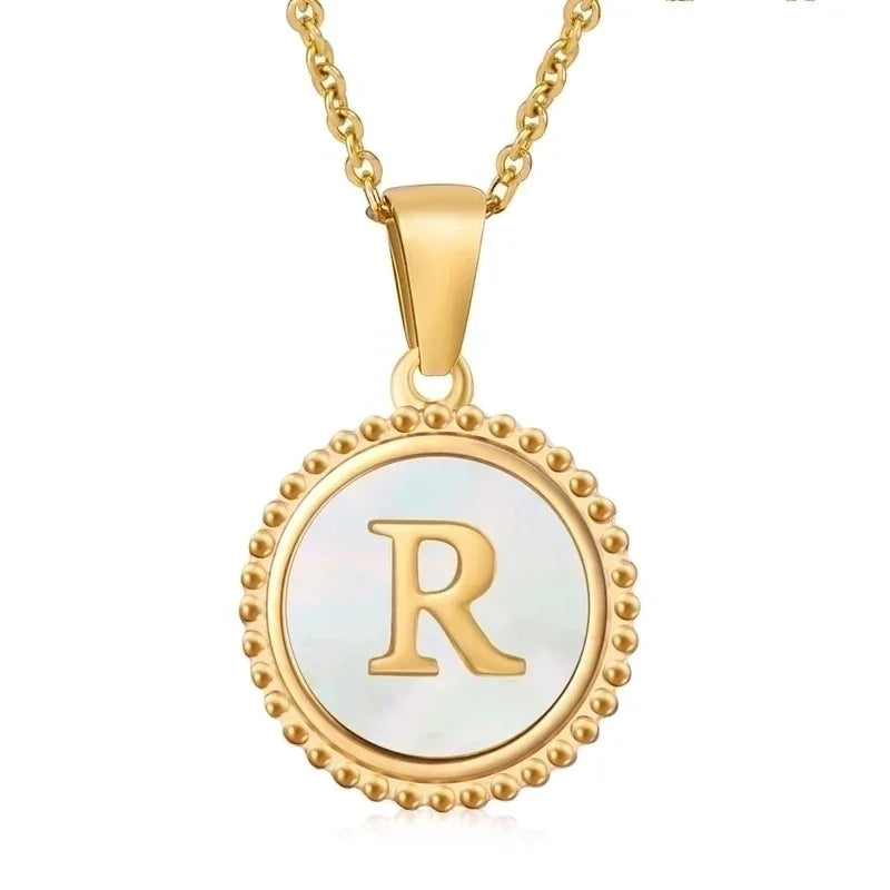 Hanger met vergulde ketting met de letter ’R’ op een parelmoeren achtergrond met kralenrand.